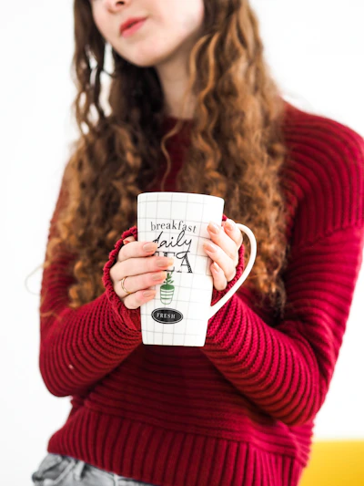 A cozy scene with a person wearing a vivaarco pride sweatshirt, holding a coffee mug with a rainbow heart.