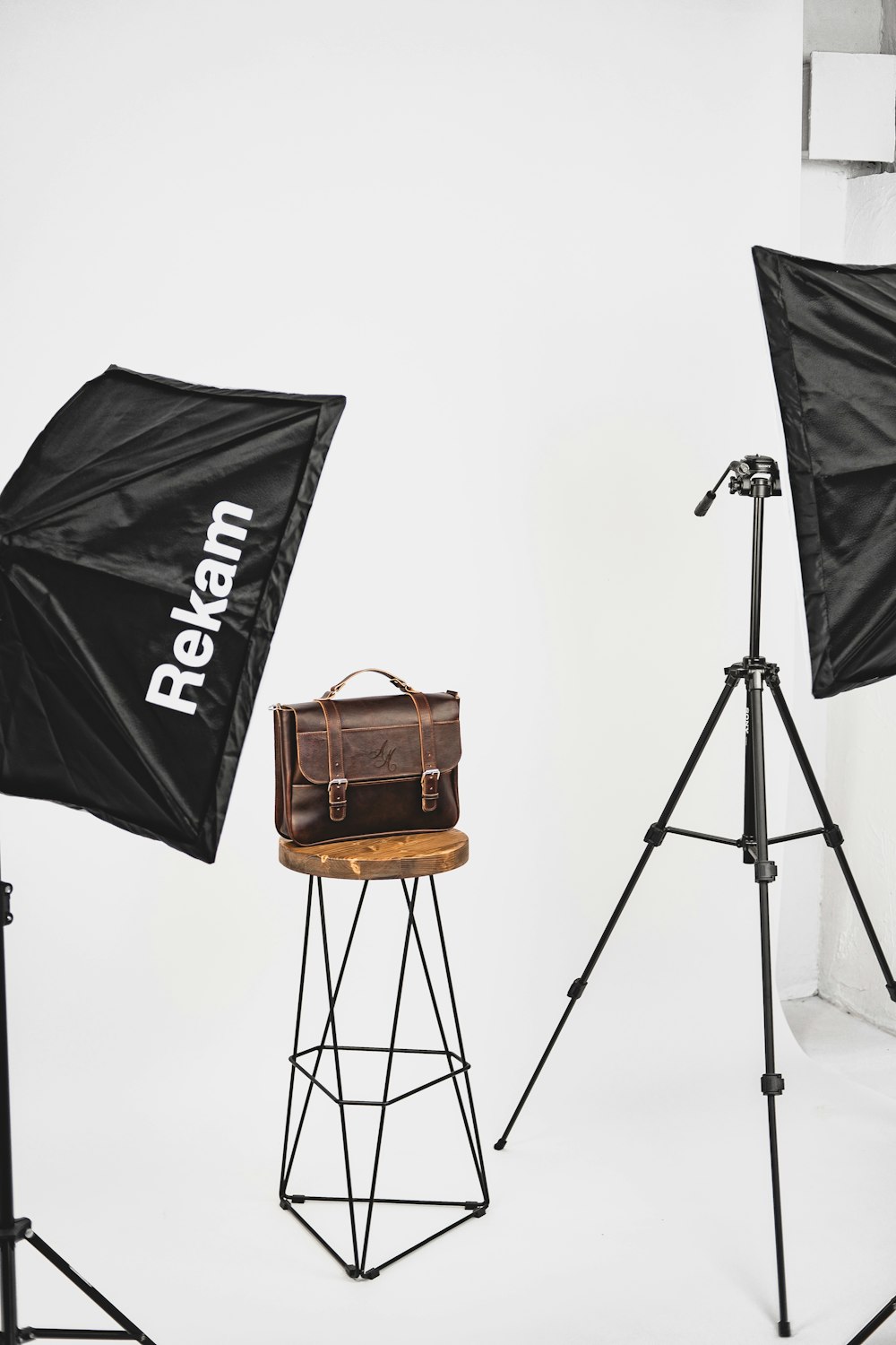 black and brown camera tripod with brown leather shoulder bag on brown wooden table