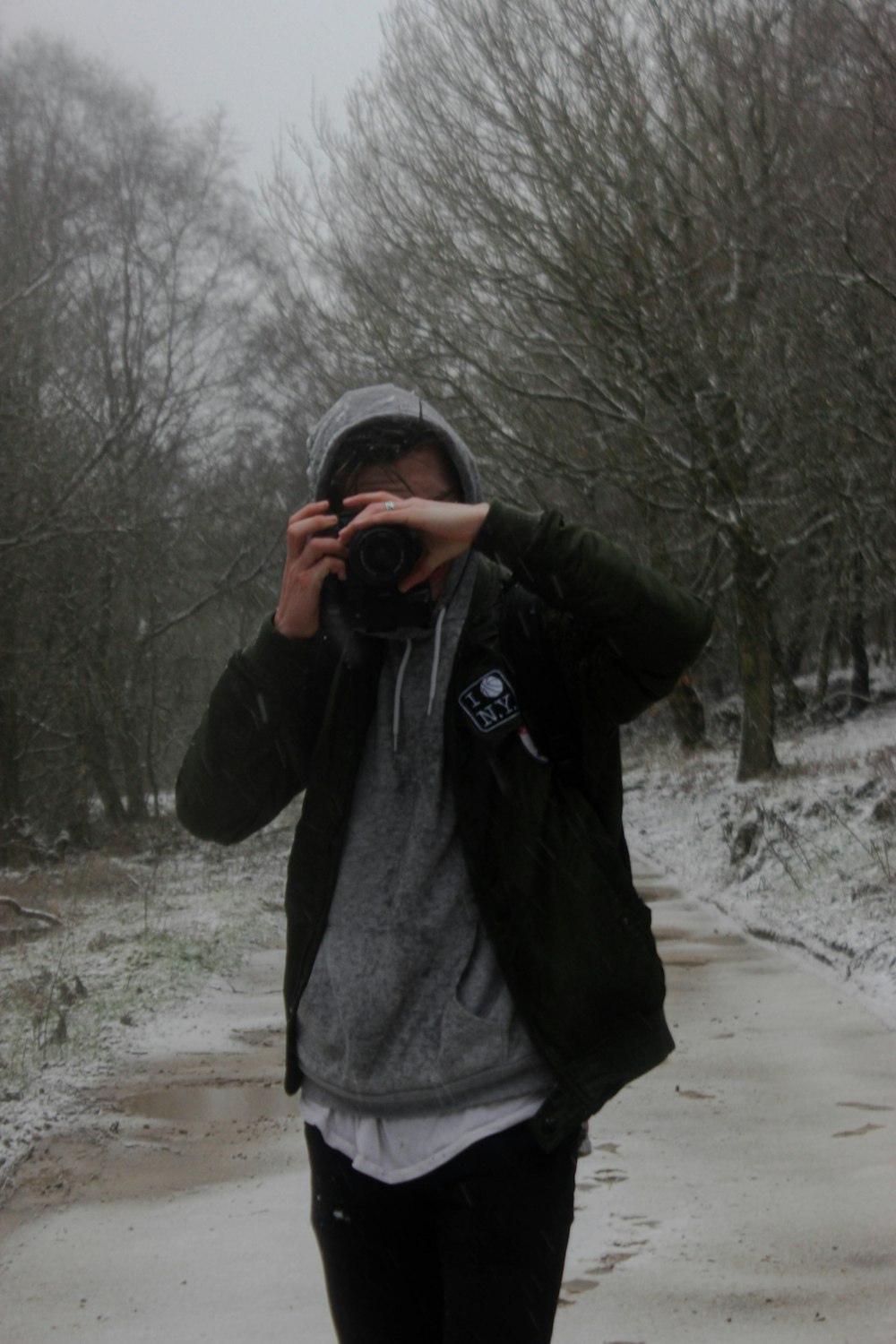 homem em jaqueta preta tirando foto de árvores nuas durante o dia