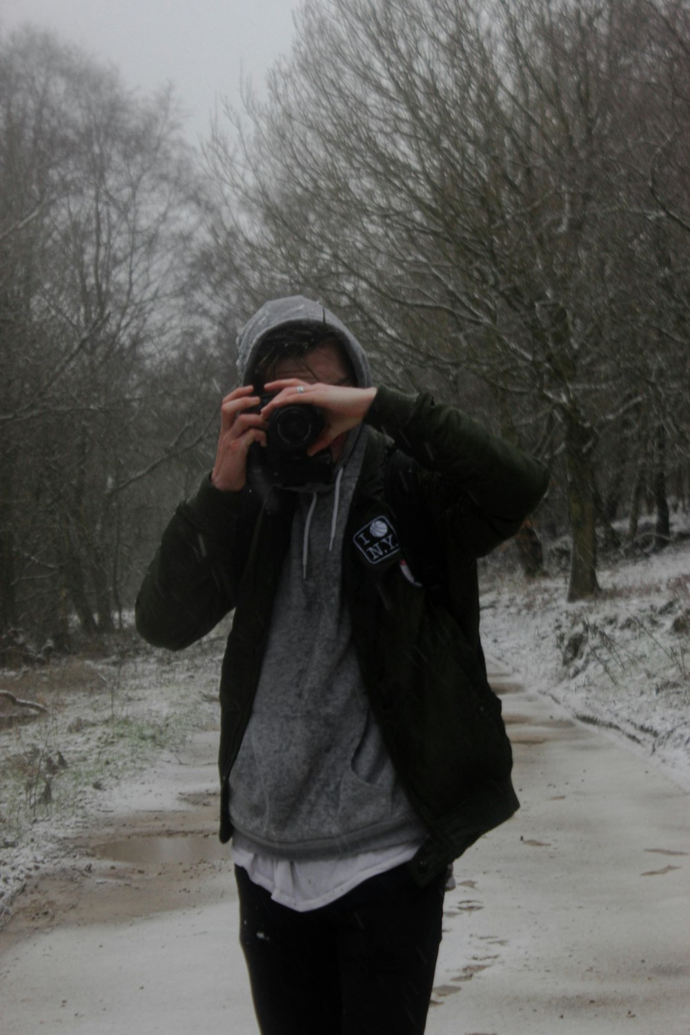 man in black jacket taking photo of bare trees during daytime