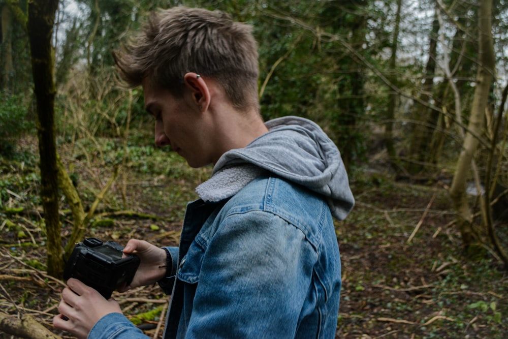 man in blue denim jacket and gray knit cap holding black smartphone