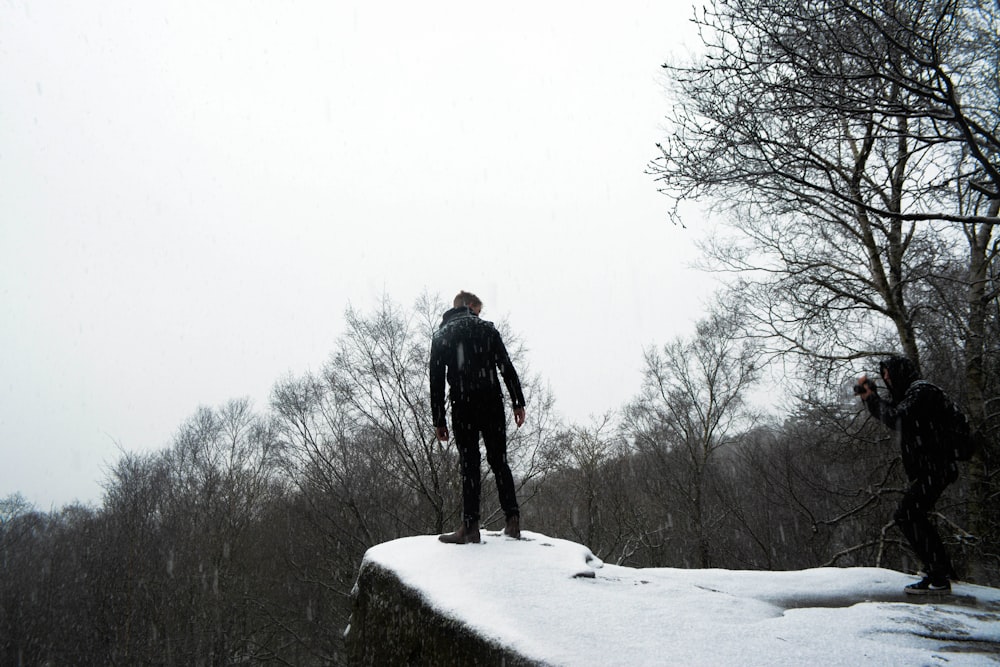 uomo in giacca nera in piedi su terreno coperto di neve durante il giorno