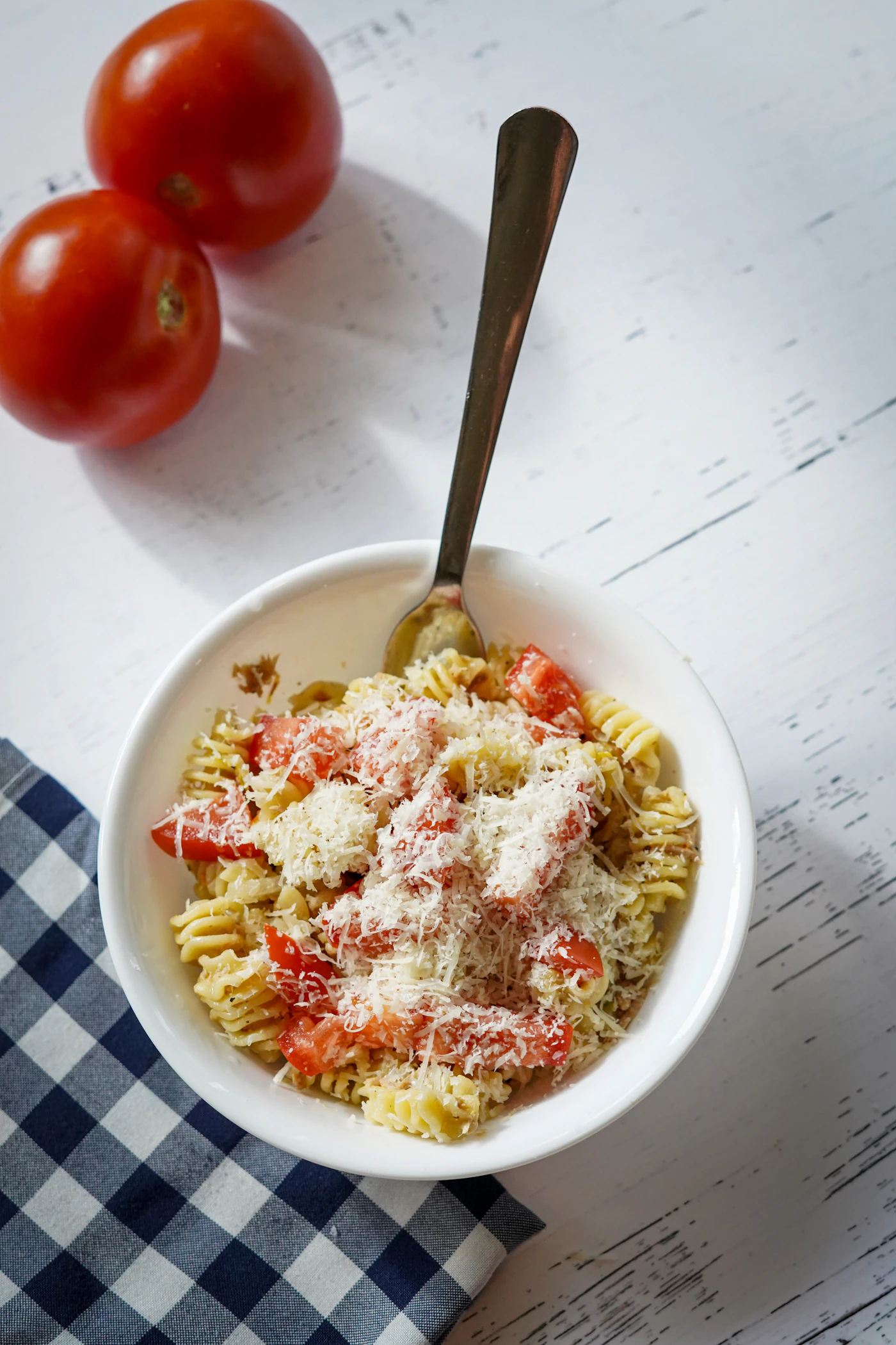 Tomato tuna pasta twirled in a white bowl with herbs and grated topping