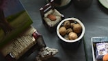 A collection of objects is arranged on a table, including a small container filled with walnuts, a miniature decorative chair, and a textured object resembling coral. There are also various painted and crafted items with intricate designs.
