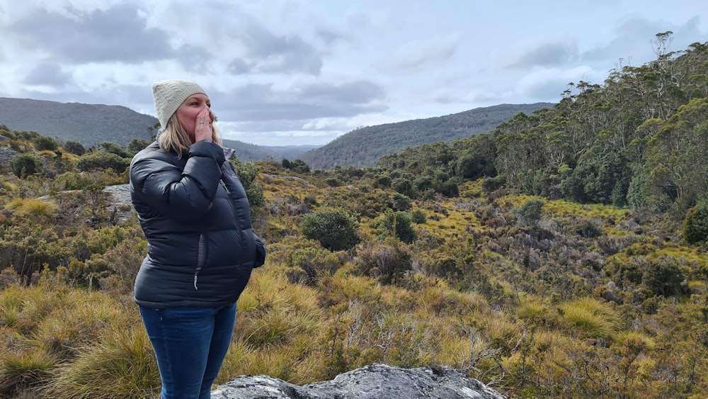 woman in black jacket and blue denim jeans standing on rock formation during daytime