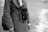 A person wearing a houndstooth patterned coat holds a vintage twin-lens reflex camera hanging from their neck. The image is in black and white, capturing a classic and timeless feel. The background is blurred, focusing on the detailed textures of the coat and the camera.