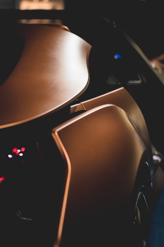 A sleek, futuristic car is shown with a focus on its elegant curves and smooth, metallic bronze surface. The image captures part of the car's rear, emphasizing its streamlined design and the subtle play of light and shadow on the bodywork.