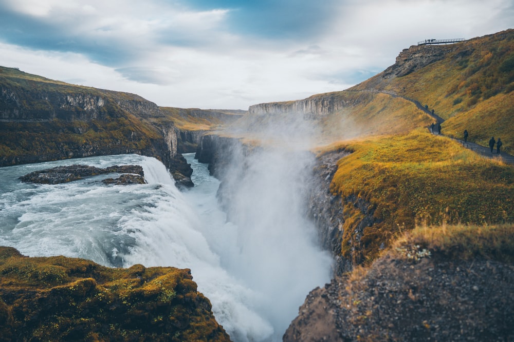 water falls on brown and green mountain under white clouds during daytime