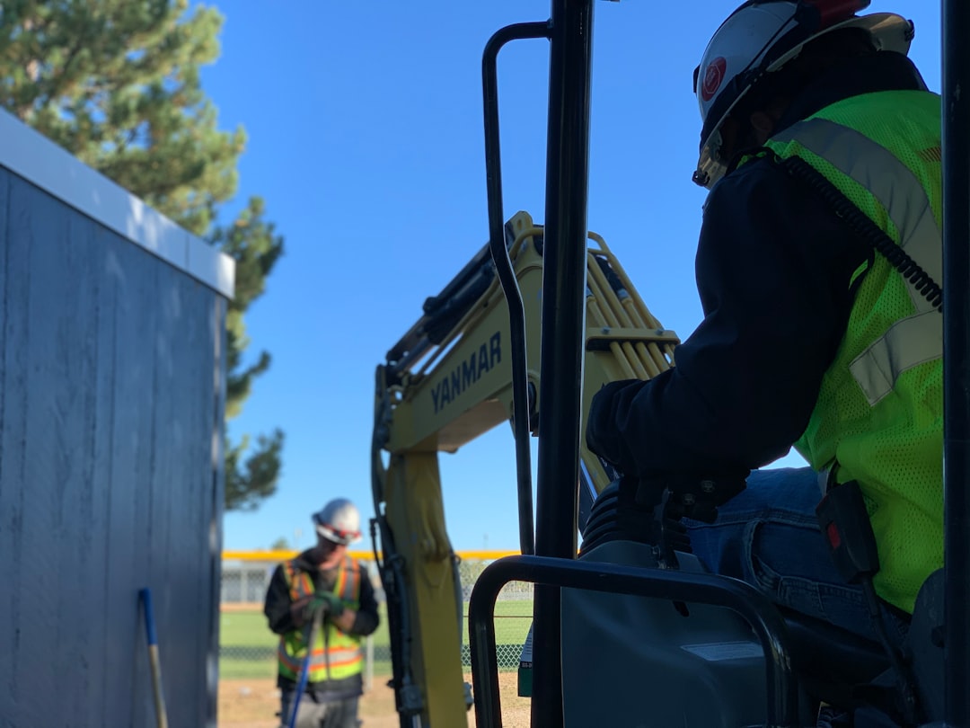 man in black jacket and helmet riding on black tractor during daytime, Construction worker operating an excavator digging a trench on a construction site