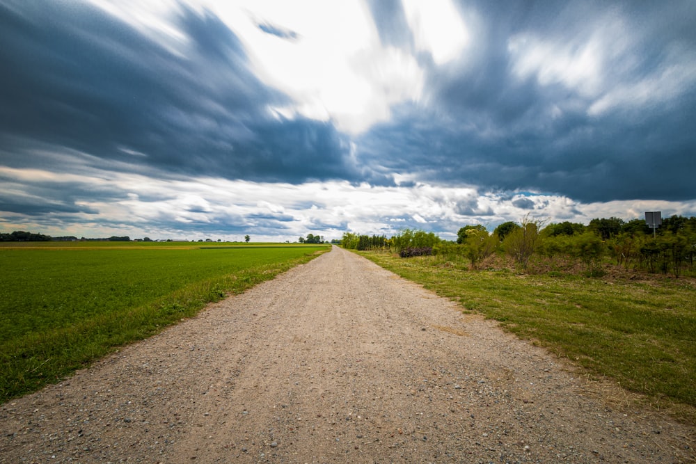 brown dirt road between green grass field under blue and white cloudy sky during daytime