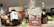 An assortment of groceries and items are placed on a countertop. There are various fruits like apples and avocados in a bowl, a package of tortillas, a box of Hello Panda chocolate snacks, a bottle of supplements, and several bottles of beverages including wine and liqueur. Additionally, a package of kitchen sponges is visible.