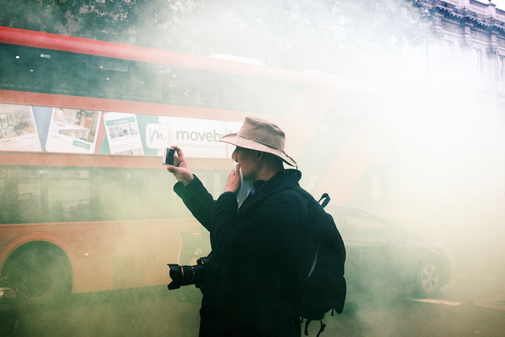 man in black jacket and brown hat holding black dslr camera