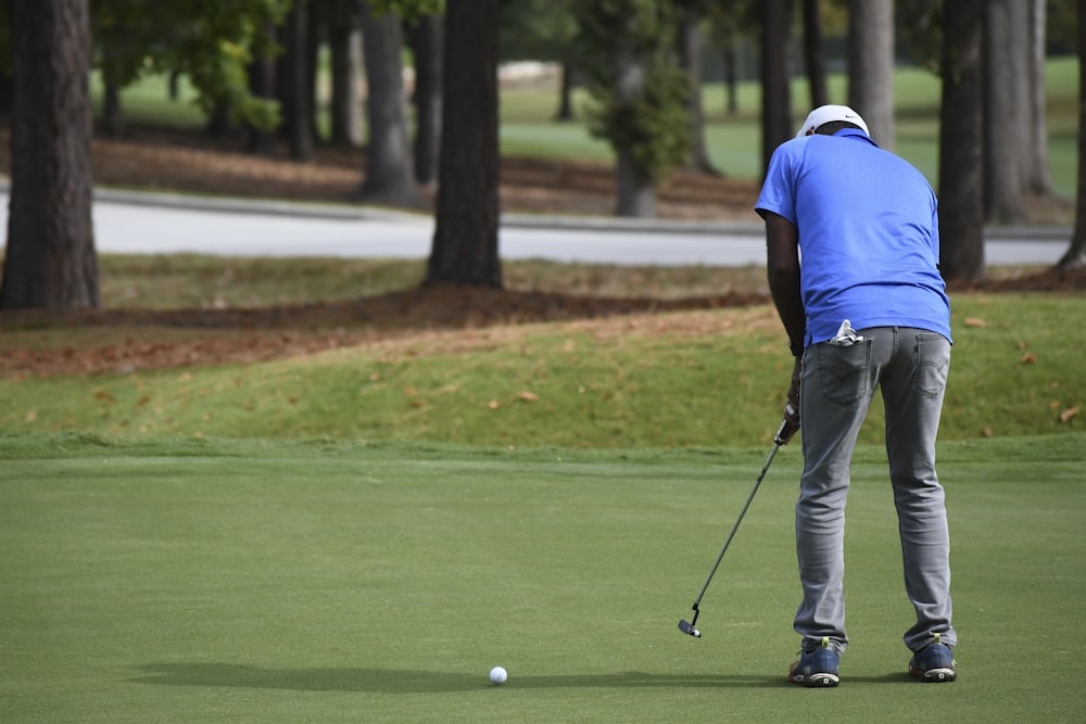 homem na camisa polo azul e calças cinzas jogando golfe durante o dia