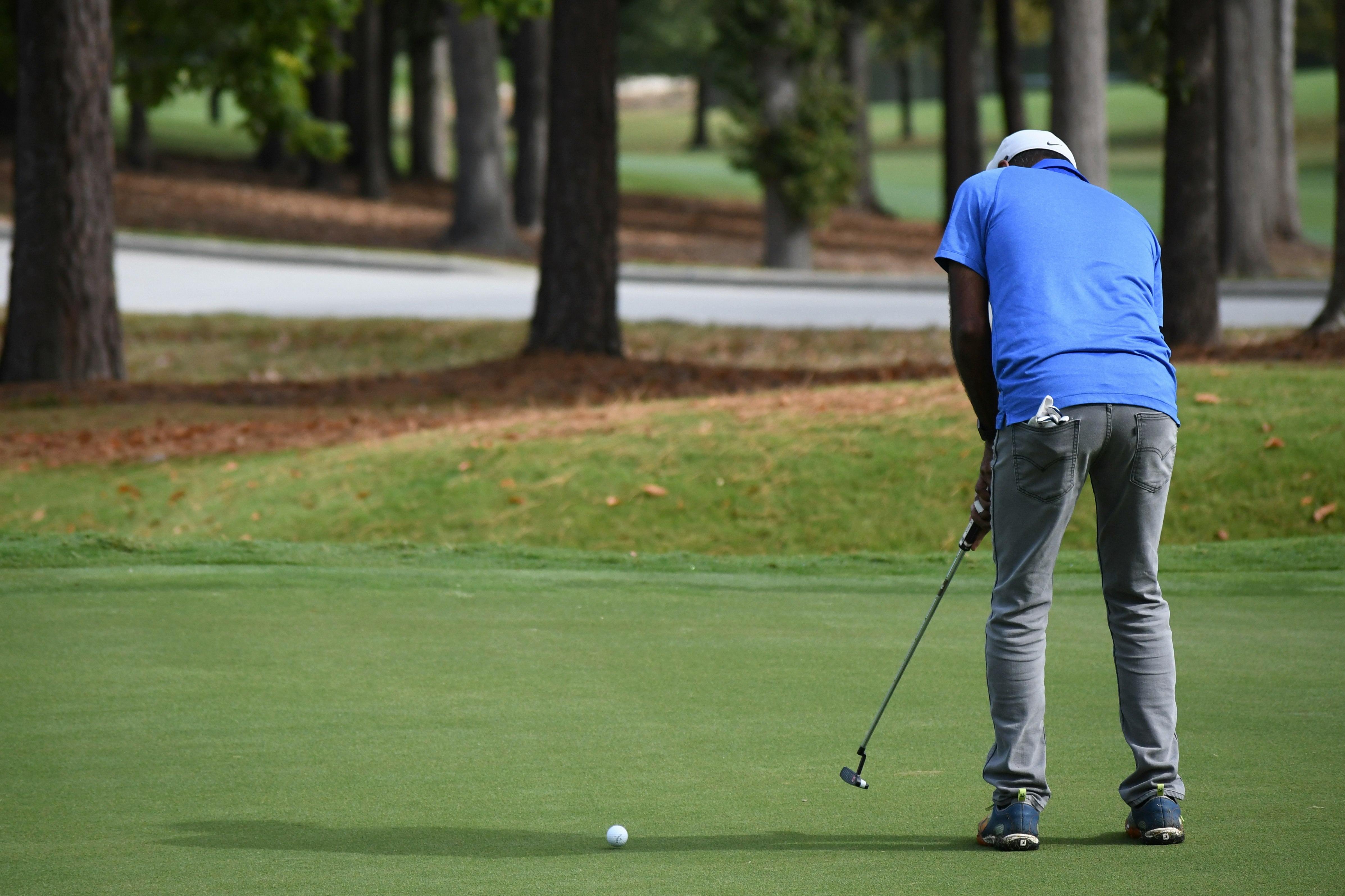 man in blue polo shirt and gray pants playing golf during daytime