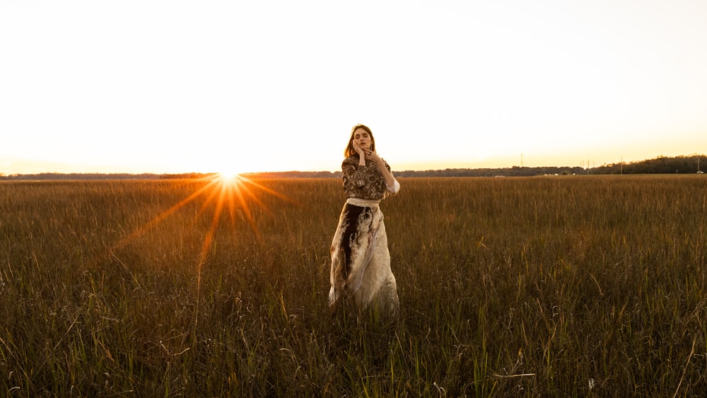 mulher no vestido branco que está no campo verde da grama durante o pôr do sol