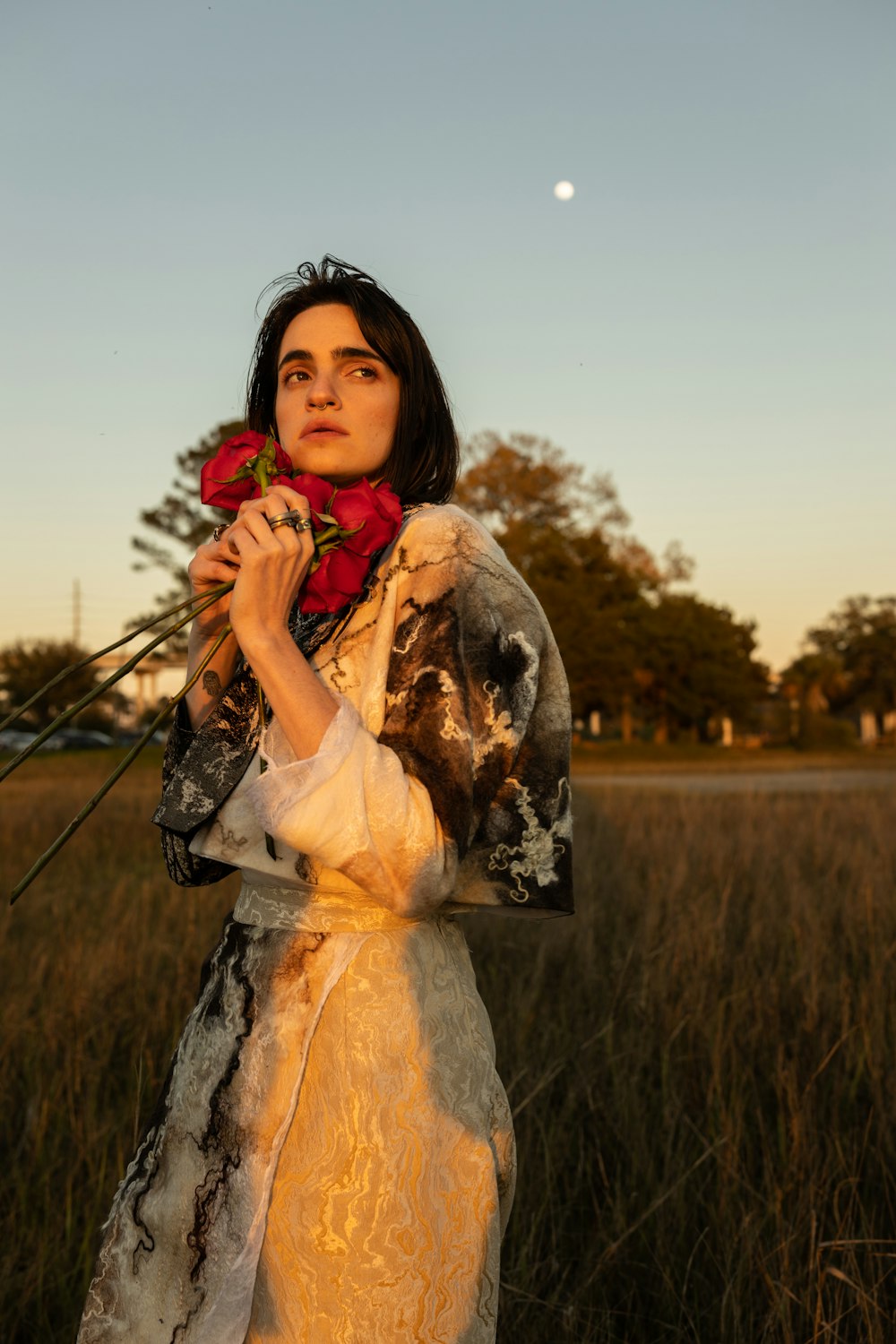 woman in white and brown floral long sleeve dress holding red flower