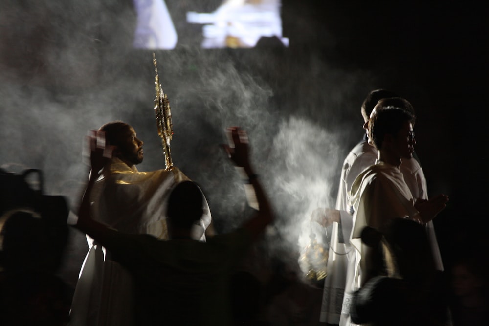 3 men in white robe holding brass trumpet