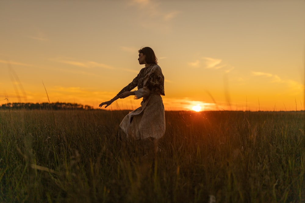 Frau in weißem Kleid steht bei Sonnenuntergang auf grünem Grasfeld