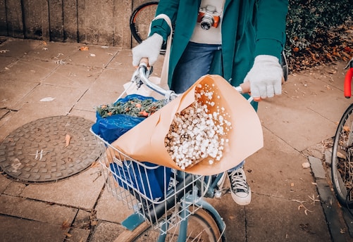 A delivery person carrying a vibrant bouquet of flowers on a bike through a sunny neighborhood.