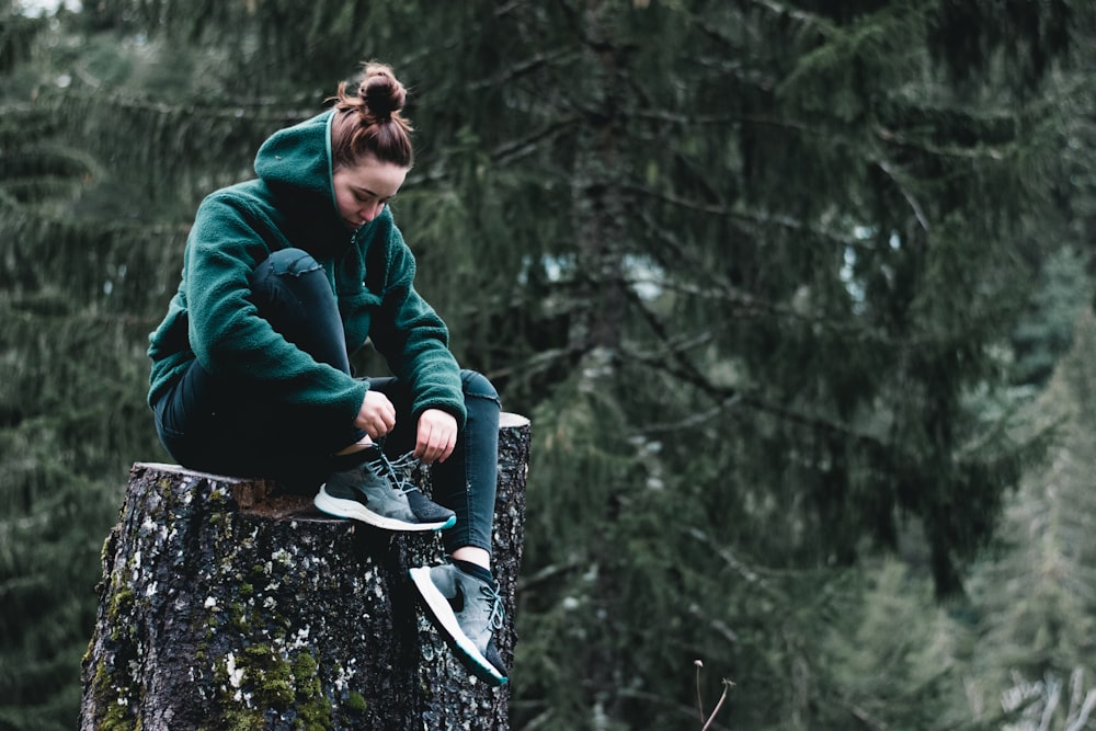 Mujer en chaqueta verde sentada en el tronco de un árbol