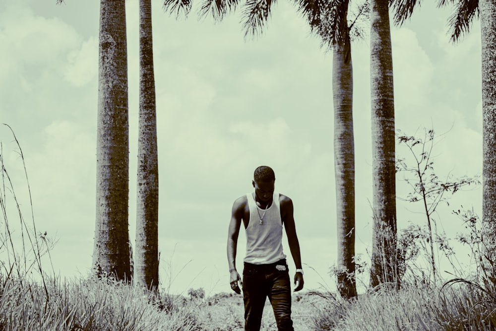 man in white tank top and black pants standing near palm trees