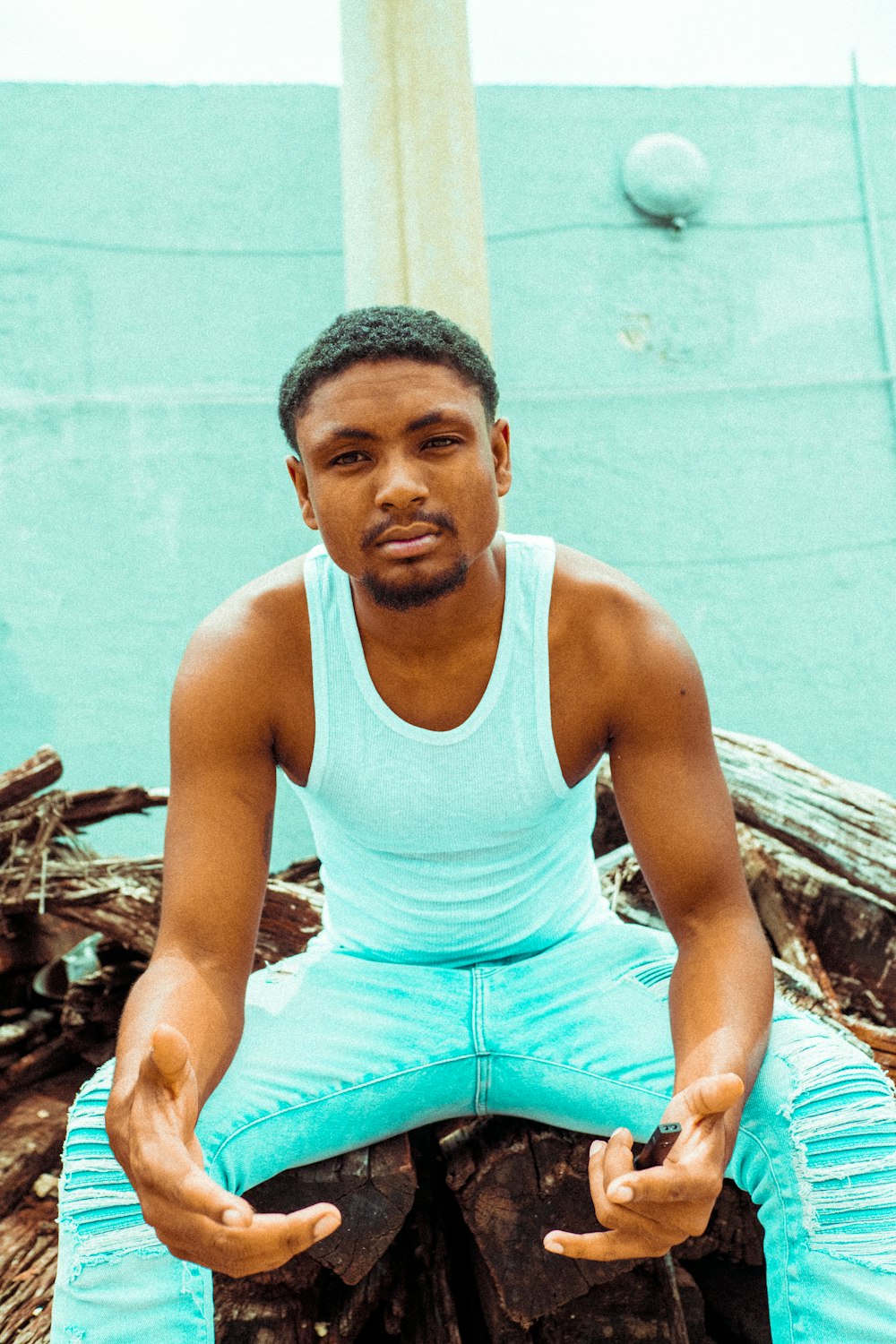 man in white tank top and blue shorts sitting on brown wooden log