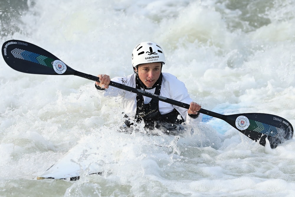 man in black jacket and white helmet riding on black kayak on body of water during