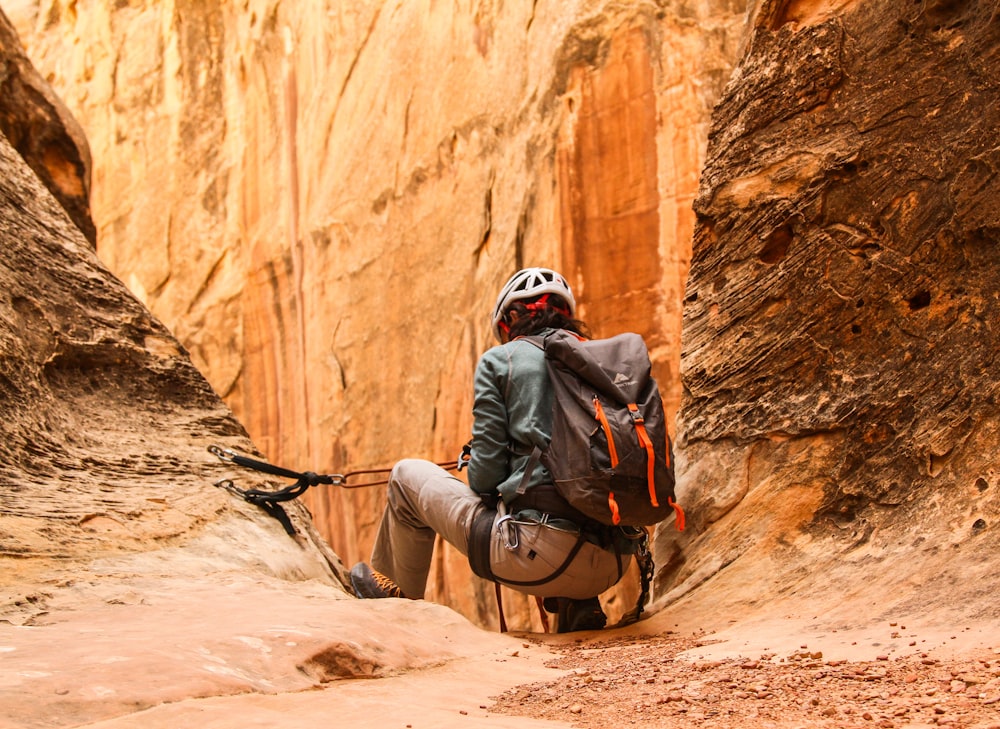 man in gray jacket and black helmet sitting on brown rock formation during daytime