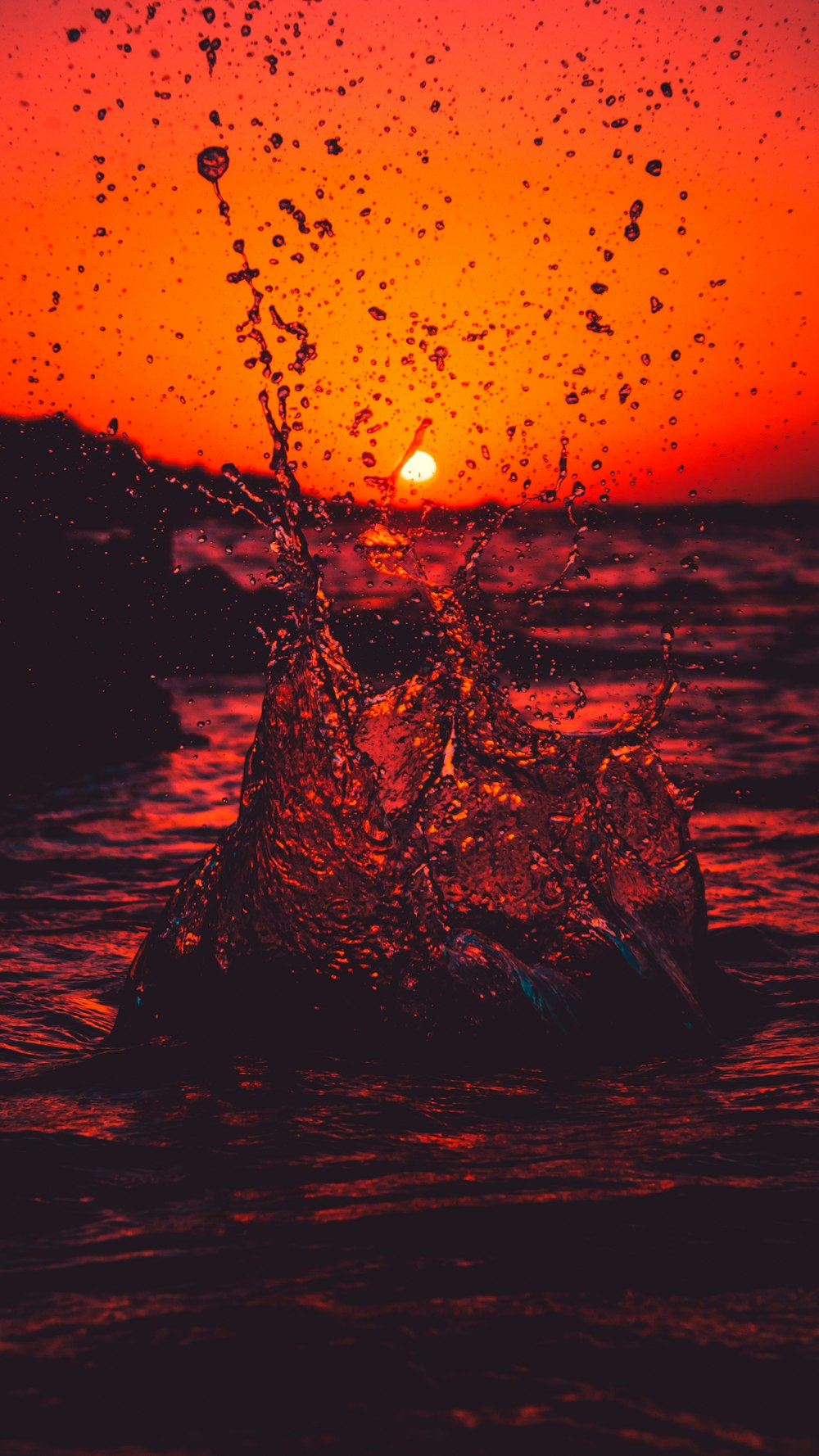 Spruzzi d'acqua sulla roccia nera durante il tramonto