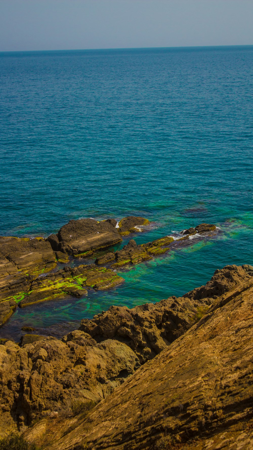 Formación rocosa verde y marrón junto al mar azul durante el día