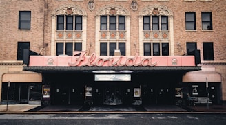 The image features a historic theater facade with ornate architectural details, highlighted by a large, retro-style marquee that spells 'Florida'. The building is constructed from red brick, and intricate designs adorn the upper level above the entrance.