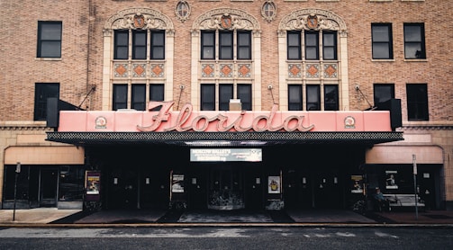 The image features a historic theater facade with ornate architectural details, highlighted by a large, retro-style marquee that spells 'Florida'. The building is constructed from red brick, and intricate designs adorn the upper level above the entrance.