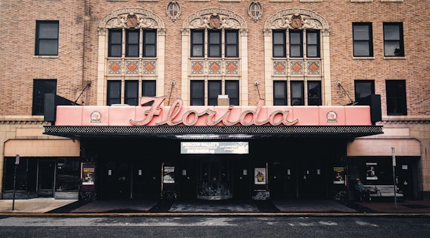 The image features a historic theater facade with ornate architectural details, highlighted by a large, retro-style marquee that spells 'Florida'. The building is constructed from red brick, and intricate designs adorn the upper level above the entrance.