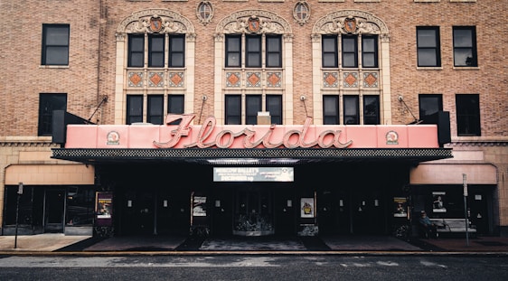 The image features a historic theater facade with ornate architectural details, highlighted by a large, retro-style marquee that spells 'Florida'. The building is constructed from red brick, and intricate designs adorn the upper level above the entrance.
