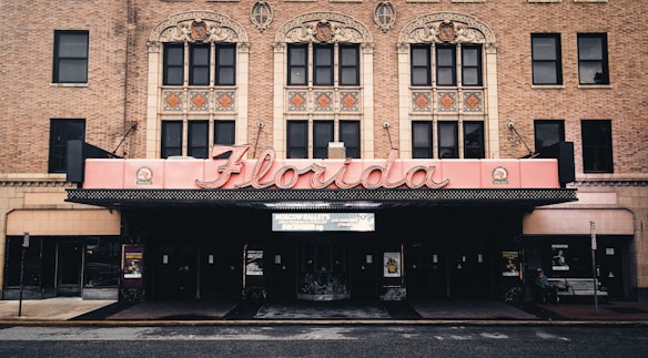 The image features a historic theater facade with ornate architectural details, highlighted by a large, retro-style marquee that spells 'Florida'. The building is constructed from red brick, and intricate designs adorn the upper level above the entrance.