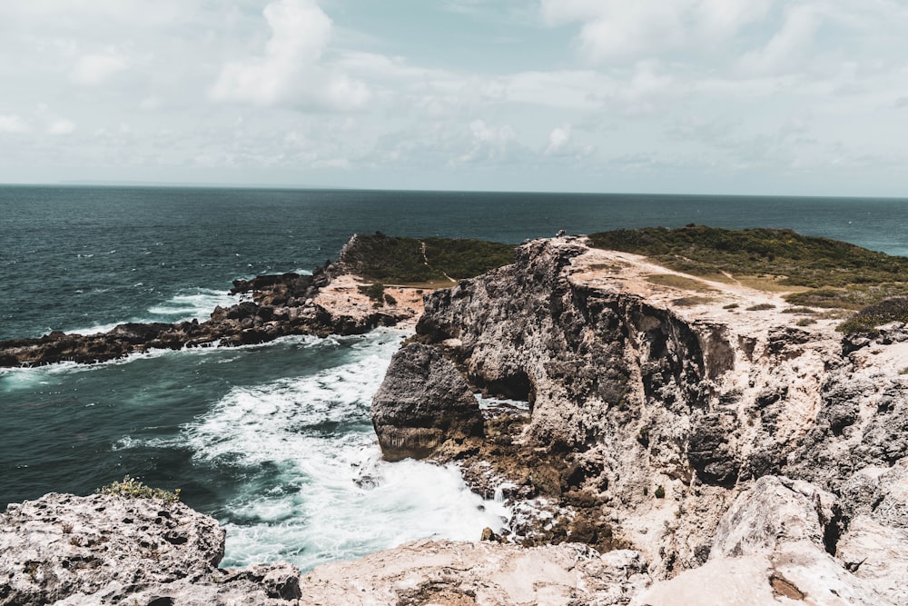 brown rocky mountain beside blue sea under white clouds and blue sky during daytime