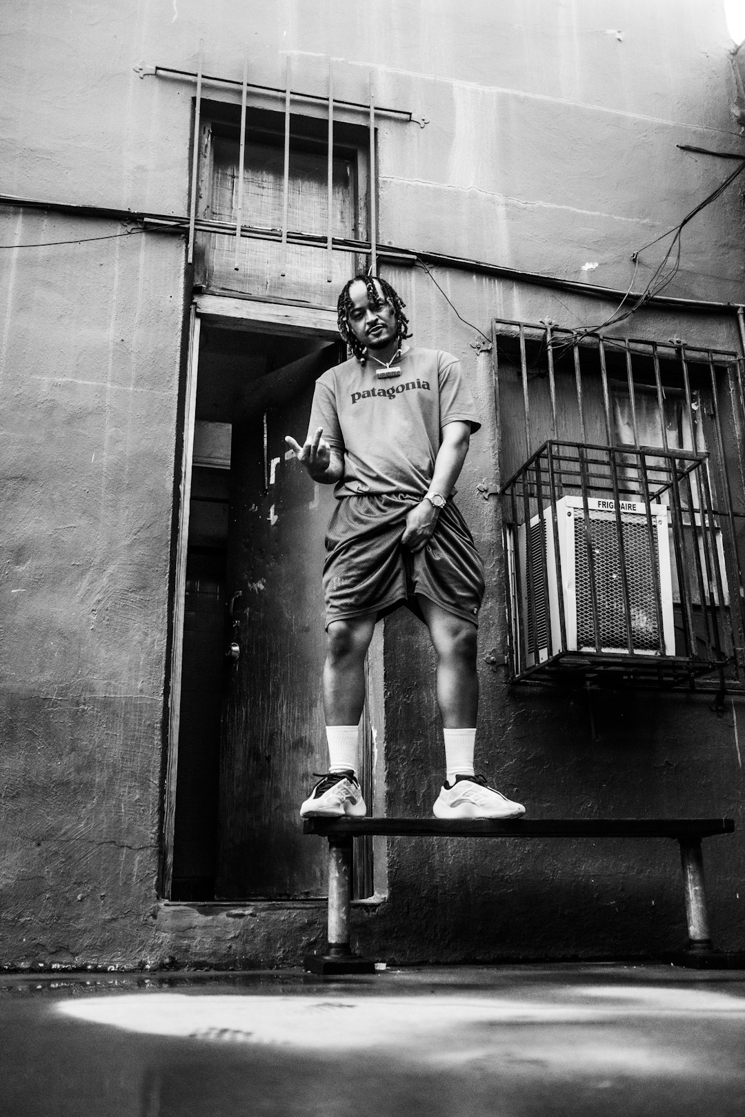 grayscale photo of man in t-shirt and shorts sitting on bench