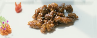 A plate of glazed, crispy fried chicken pieces garnished with a small flower arrangement and a carrot shaped like a rabbit.