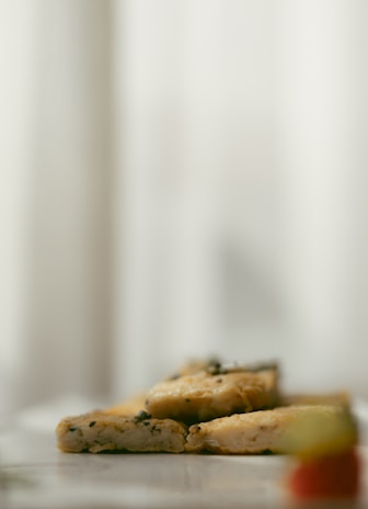 Slices of grilled or roasted tofu, garnished with herbs, arranged on a white plate with a blurred background.