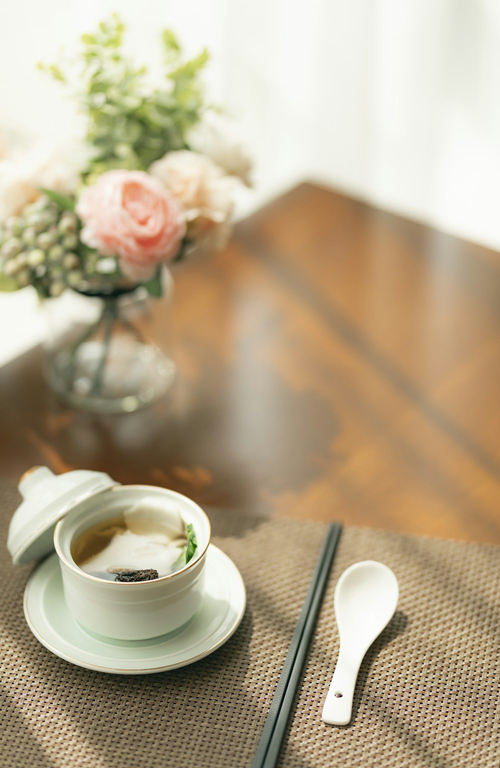 weiße Keramiktasse auf weißer Untertasse neben Edelstahllöffel auf braunem Holztisch