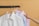 Three neatly pressed shirts in white, blue, and pink are hanging on wooden hangers on a horizontal black rod. A hand is reaching towards the shirt in the middle.