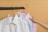 Three neatly pressed shirts in white, blue, and pink are hanging on wooden hangers on a horizontal black rod. A hand is reaching towards the shirt in the middle.