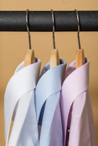 Three men's clothing items displayed on hangers against a soft blue background.