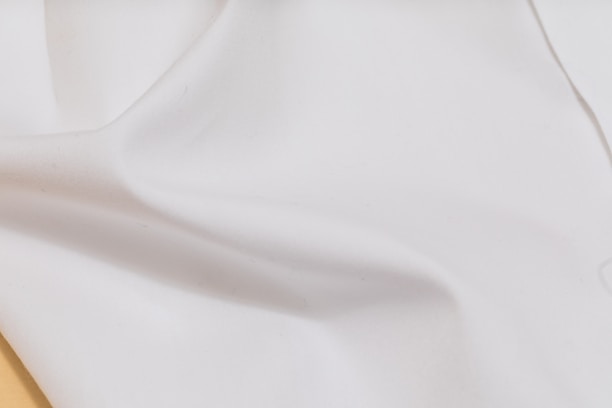 Close-up of a smooth, shimmering silk shirt draped softly on a minimalist white background.