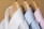 Three neatly pressed collared shirts hang on wooden hangers. The shirts are arranged closely together with a white shirt on the left, a light blue shirt in the center, and a light pink shirt on the right. The background is a soft beige color, creating a neutral and soothing setting.