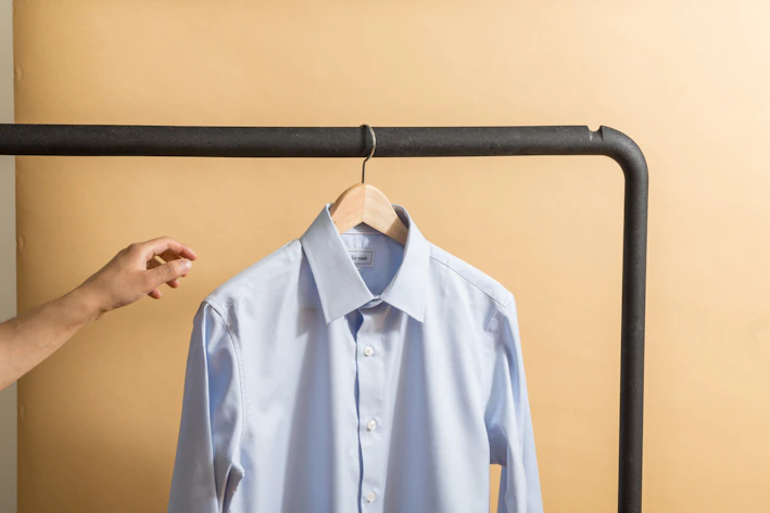 A stylish men's casual shirt in soft fabric displayed on a wooden hanger against a blue background.