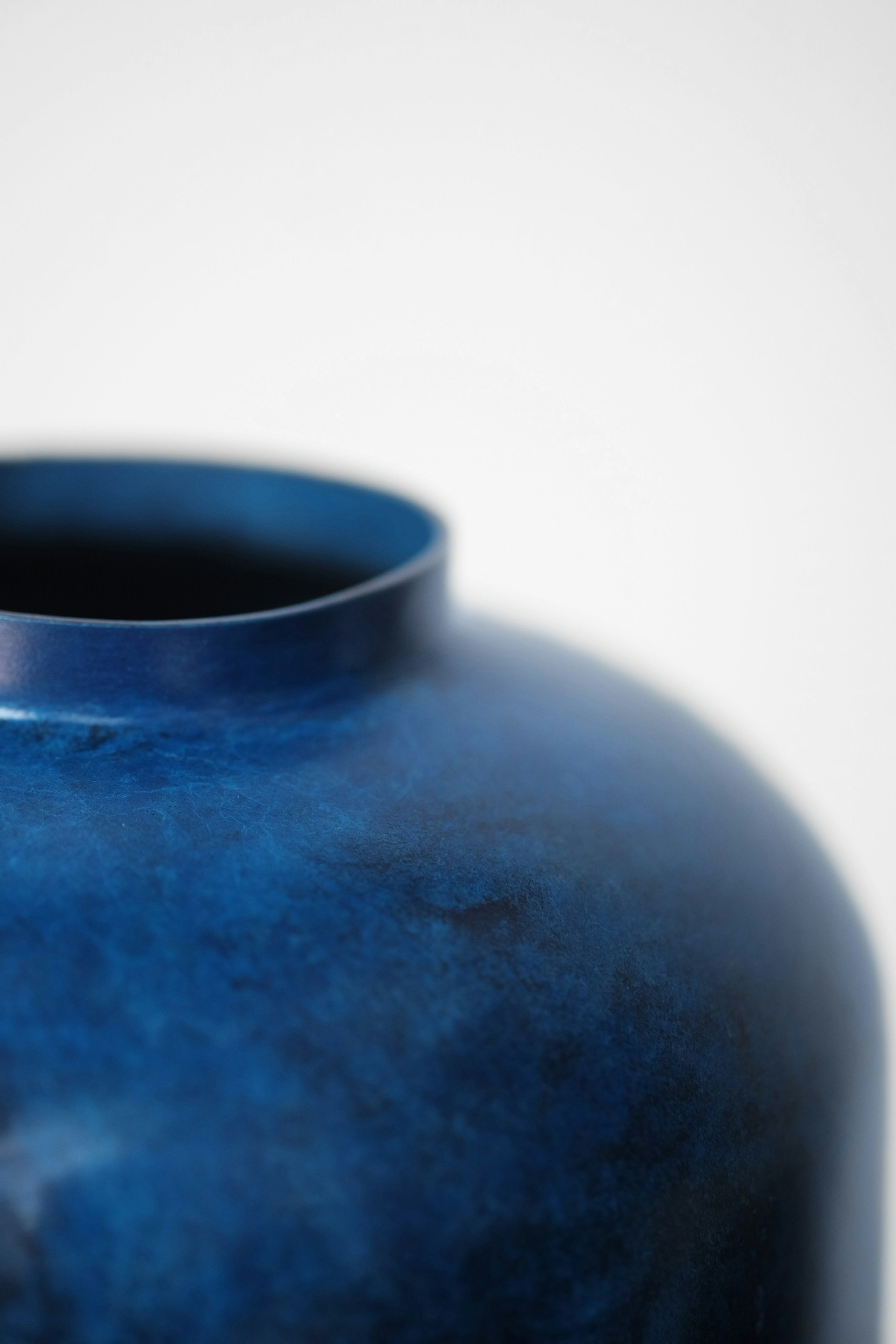 A close-up of a handmade stoneware vase glazed in deep blue hues, showcasing subtle texture and craftsmanship.