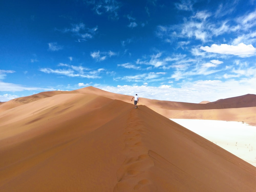 person in white shirt walking on desert during daytime