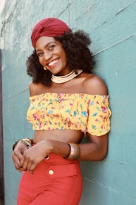 woman in yellow and red floral off shoulder dress leaning on blue wall