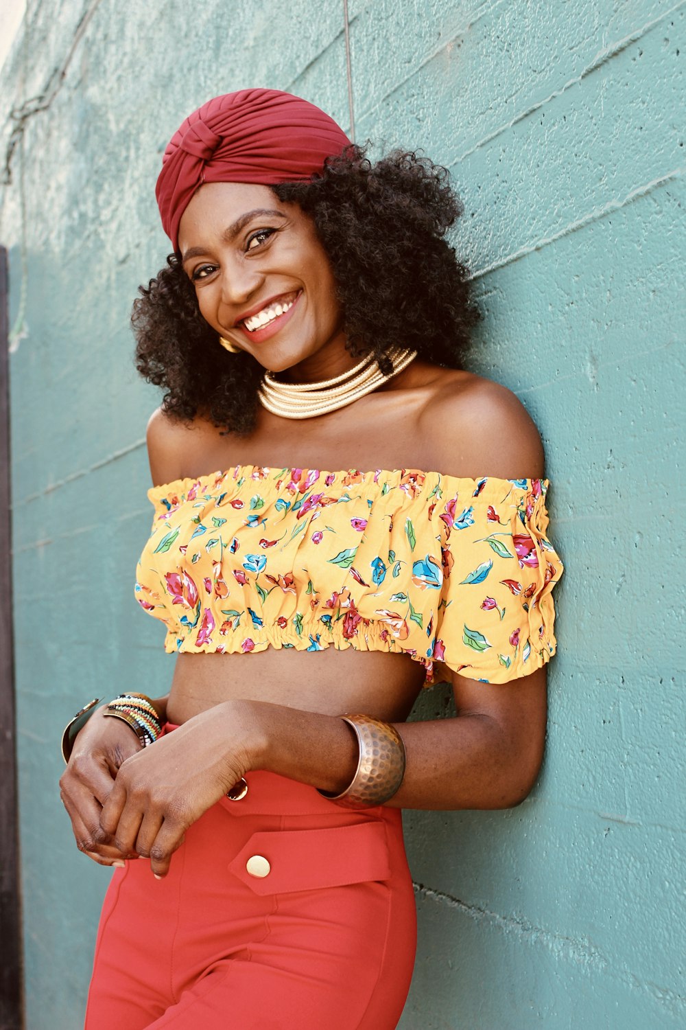 woman in yellow and red floral off shoulder dress leaning on blue wall